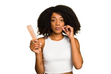 Fototapeta na wymiar Young african american woman holding hair comb isolated with fingers on lips keeping a secret.