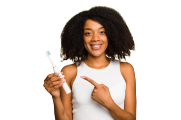 Young african american woman holding an electric toothbrush isolated smiling and pointing aside, showing something at blank space.