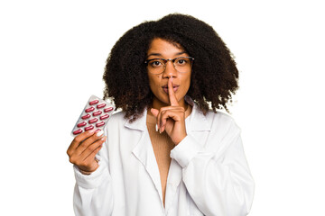 Young pharmacist African American woman holding a tablet of pills isolated keeping a secret or asking for silence.