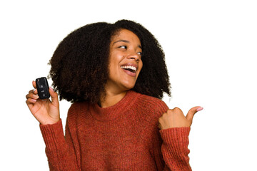 Young African american woman holding car keys isolated points with thumb finger away, laughing and...