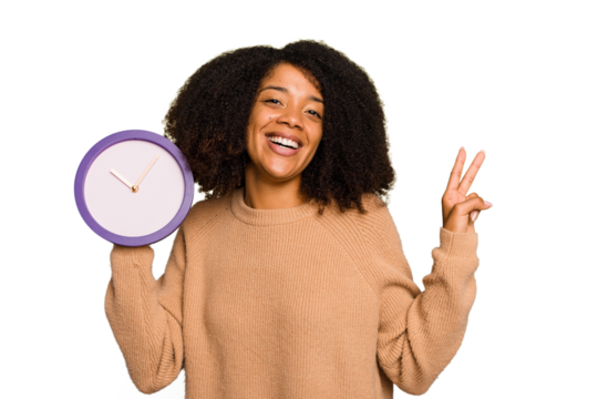 Young African American holding a clock isolated joyful and carefree showing a peace symbol with fingers.