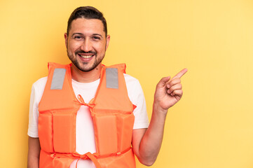 Young latin beach watcher wearing a lifejacket isolated smiling and pointing aside, showing...