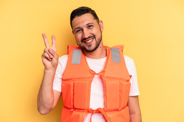 Young latin beach watcher wearing a lifejacket isolated joyful and carefree showing a peace symbol...