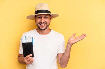 Young latin man holding a flight tickets for vacations showing a copy space on a palm and holding another hand on waist.