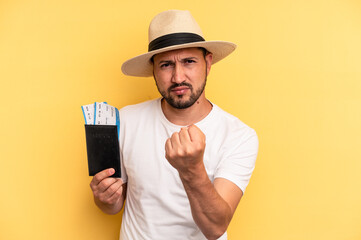 Young latin man holding a flight tickets for vacations showing fist to camera, aggressive facial expression.