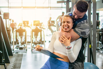 Muscular fit man choking a young female personal trainer with his arm muscle at the gym. Friends...