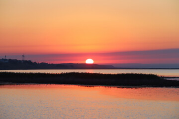 Naklejka premium A big sun rises over the bay and hills on a summer morning. Beautiful sunrise landscape. Nature background