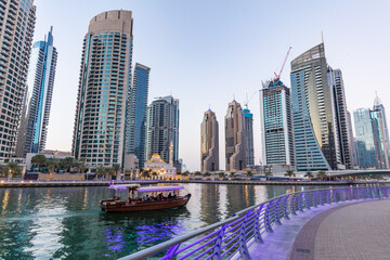 Dubai marina promenade and tourist boat in UAE at sunset.