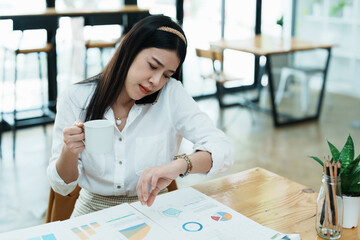 A portrait of a beautiful Asian employee hustle rushing while watch at the clock and talking on the...