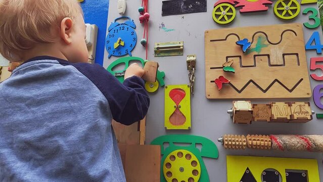 A happy child plays with educational toys in the playground in summer. Wooden game board. Copy space - entertainment concept, bright board for children, kindergarten, fine motor skills of fingers