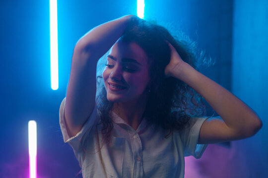 Portrait of a happy young woman dancing over neon light background at disco party