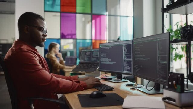 African American Man Writing Code on Desktop Computer With Multiple Monitors Set Up and a Laptop in Creative Office. Professional Data Scientist Using Software to Analyze Information From Internet.