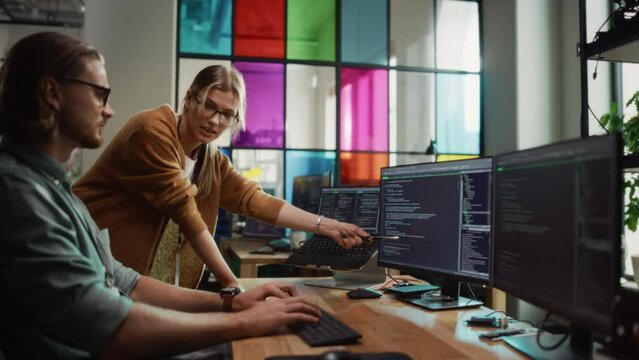 Male Programmer Shows Progress to Female Start-Up CEO on Desktop Computer in Creative Office Space. Caucasian Man and Woman Discussing New Features For Artificial Inteligence Software.