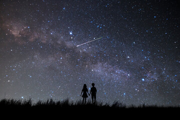 天の川と満天の星空を見つめるカップルのシルエット。