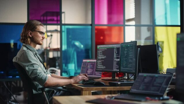 Caucasian Man Writes Code on Desktop Computer With Professional Multiple Monitors Setup in Modern Office. Male Data Scientist Using Software to Collect and Analyze Information From Opened Sources.