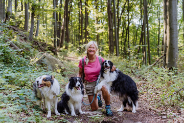 Naklejka na ściany i meble Senior woman walking with her three dogs in forest.