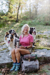 Senior woman having break during walking her three dogs in forest.