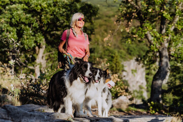 Senior woman walking with her three dogs in forest.
