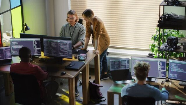 Creative Office: Diverse Colleagues Coding on Desktop Computers With Multiple Monitors. Female Project Manager Talks to Male Team Lead While Junior Developers Working on Mobile Application.