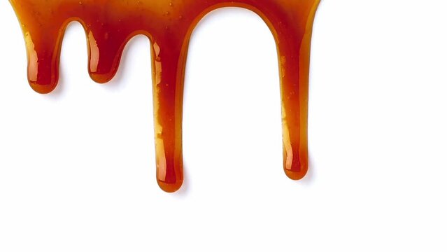 Dripping caramel drops of sweet caramel sauce. Melted caramel sauce. Pouring over white surface. 