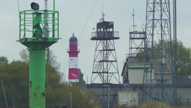 Red painted harbor lighthouse at Port of Liepaja (Latvia) on a overcast day, distant view, green port navigation beacon in foreground, communication towers, medium shot