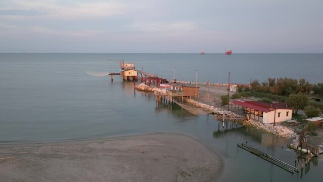 Slow-motion aerial view of fishing huts on shores of estuary at sunset,italian fishing machine, called ""trabucco"",Lido di Dante, Ravenna near Comacchio valley.