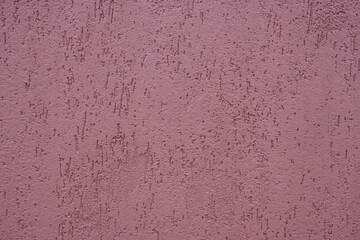 Closeup of plastered exterior wall painted in mauve purple color. Indented texture background.