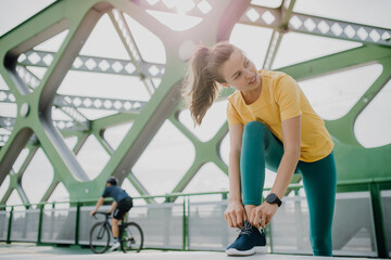 Portrait of young sportive woman resting outdoor during city run, tiing her shoelaces.