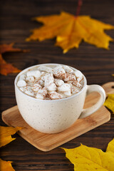 Cocoa with marshmallows in a mug on a wooden board with autumn leaves.