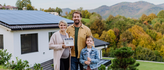 Happy family holding paper model of house with solar panels.Alternative energy, saving resources...