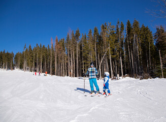 Happy little boy learns to ski with his father during winter holidays in snowy mountains on a sunny cold day. An interesting active holiday with the family. healthy lifestyle, enjoy the moment