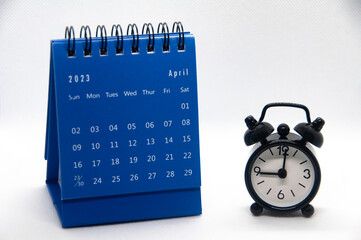 Alarm clock pointing at 9 o'clock with April 2023 calendar on white background. Time and calendar concept and copy space