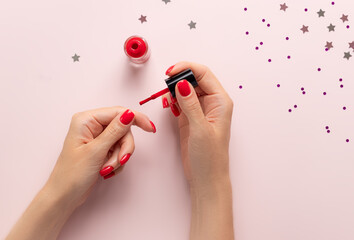 woman painting her nails with red nail polish on pink background with confetti. Home manicure. beauty treatment and hand care.