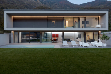 Frontal view modern house with swimming pool and garden illuminated by LED lights at dusk.