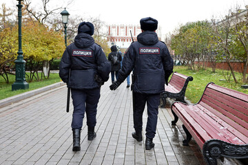Russian police officers patrol a city street in Moscow at autumn during snow. Translation of inscription on the human backs: "Police"