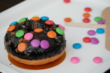 Closeup shot of a chocolate donut cake with colorful candies on it on a white desk