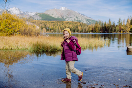 Little girl walking in the shore of lake, in the middle of beautiful autumn nature.