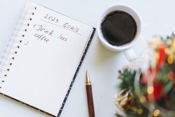 open notepad with text new year resolutions. and empty list. laptop and smartphone on background