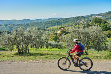 nice senior woman riding her electric mountain bike between olive trees in the Casentino hills near Arezzo,Tuscany , Italy