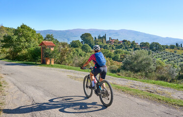 Fototapeta premium nice senior woman riding her electric mountain bike between olive trees in the Casentino hills near Arezzo,Tuscany , Italy