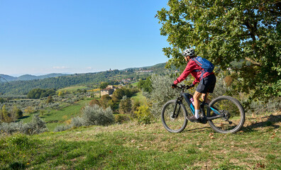 nice senior woman riding her electric mountain bike between olive trees in the Casentino hills near Arezzo,Tuscany , Italy