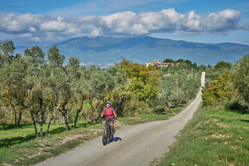 nice senior woman riding her electric mountain bike between olive trees in the Casentno hills near Arezzo,Tuscany , Italy