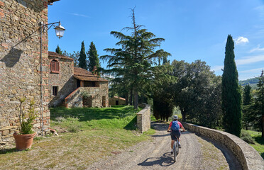 cheerful senior woman cycling with her electric mountain bike in a typical Tuscan village near...