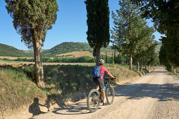 nice senior woman riding her electric mountain bike in a cypress avenue in the Chianti area near...