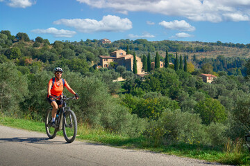 nice senior woman riding her electric mountain bike between olive trees in the Casentno hills near Arezzo,Tuscany , Italy