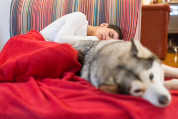 Young woman sleeping on the sofa with her pet husky dog