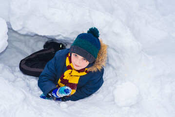 Fototapeta na wymiar happy schoolboy lies in snow cave in winter outside