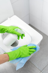 person in gloves cleaning toilet lid with cloth rag and spray in bottle