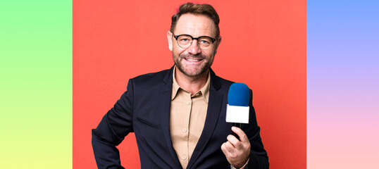 middle age man smiling happily with a hand on hip and confident. journalist and a microphone concept