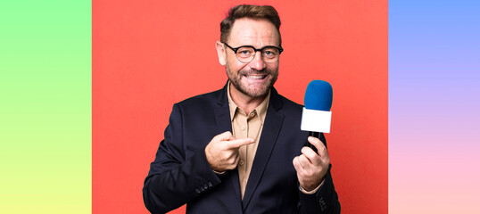 middle age man smiling cheerfully, feeling happy and pointing to the side. journalist and a...